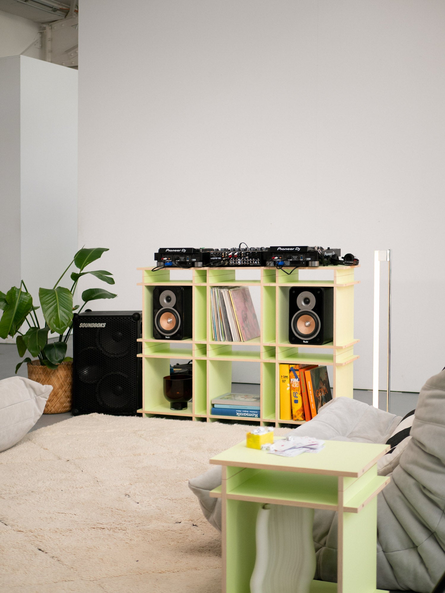 Hell Grünes Schallplattenregal aufgebaut als DJ-Setup. Große Boxen, Schallplatten und Bücher dekorieren das Regal.