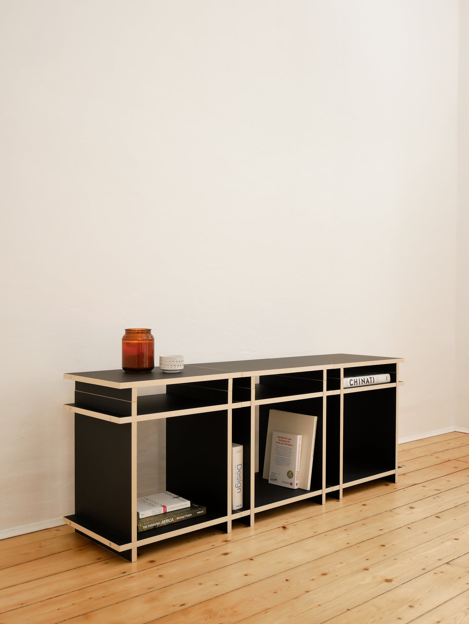 Sideboard Aufbau eines sehr reduzierten Regal, Regalsystemes von der Marke Kiyo. Vor einer weissen Wand, mit einigen wenigen Büchern dekoriert.