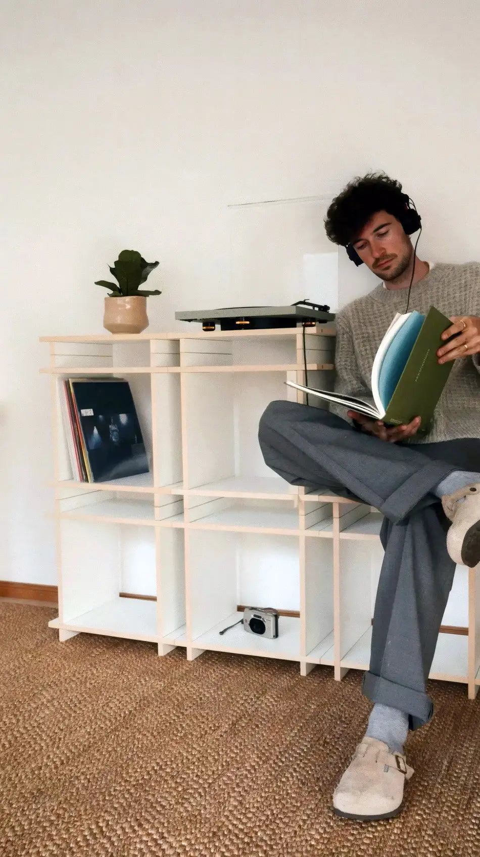 Junger Mann sitzt auf einem Sideboard-Regal und hört Musik direkt vom Schallplattenspieler.