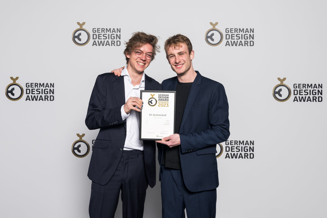 Die beiden Gründer der Kiyo GmbH vor einer hellen Fotowand halten die Urkunde des German Design Awards in der Hand, welchen sie mit dem R1 Regal, Regalsystem von Kiyo gewonnen haben