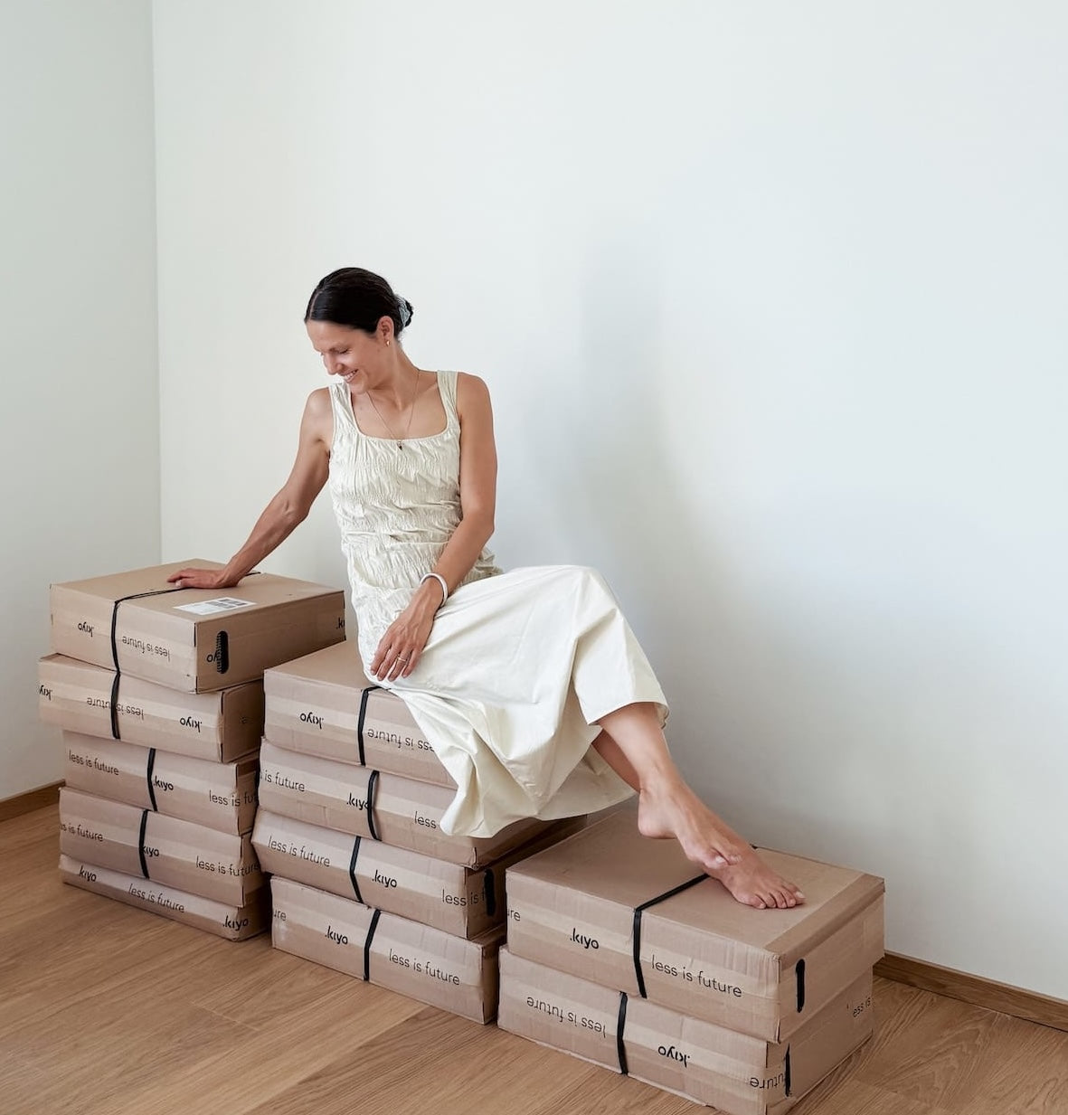 Frau sitzt auf einer Paketlieferung, in der sich Regalelemente befinden. Sie ist glücklich und freut sich auf den Aufbau.