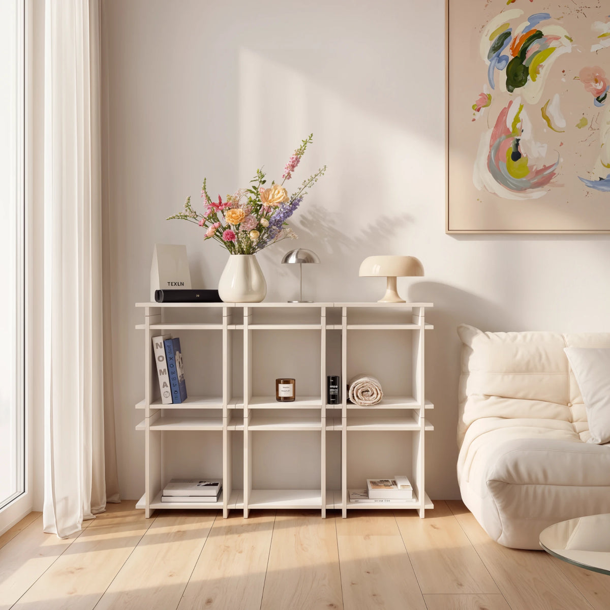 R1 Highboard Bundle in Weiß von Kiyo als Regal im Wohnzimmer, mit Blumenvase, Tischleuchten und Büchern.