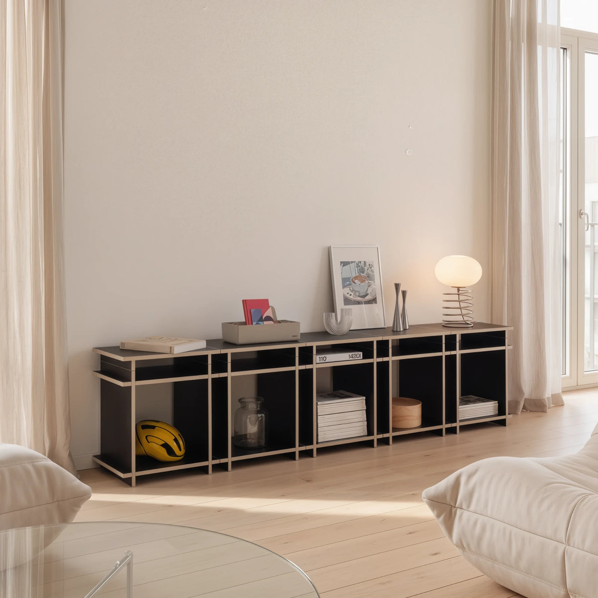 R1 Lowboard Bundle in Schwarz von Kiyo als Sideboard im Wohnzimmer, seitlich, mit Büchern, Tischleuchte und Fahrradhelm.