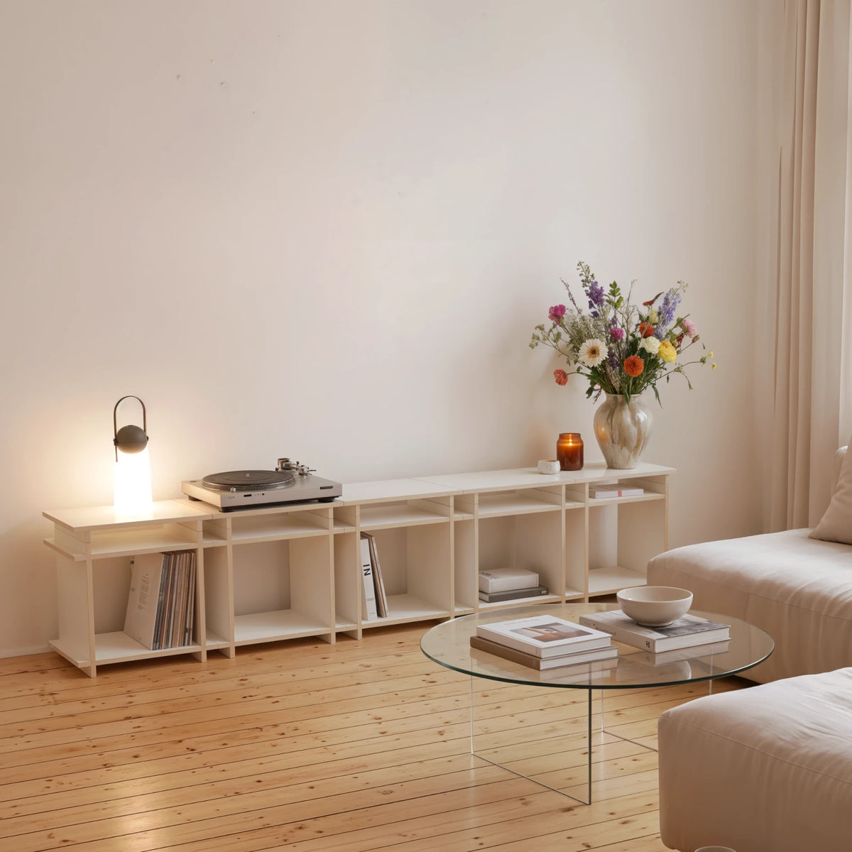 R1 Lowboard Bundle in Weiß von Kiyo mit Plattenspieler, Leuchte und Blumenstrauß im Wohnzimmer.