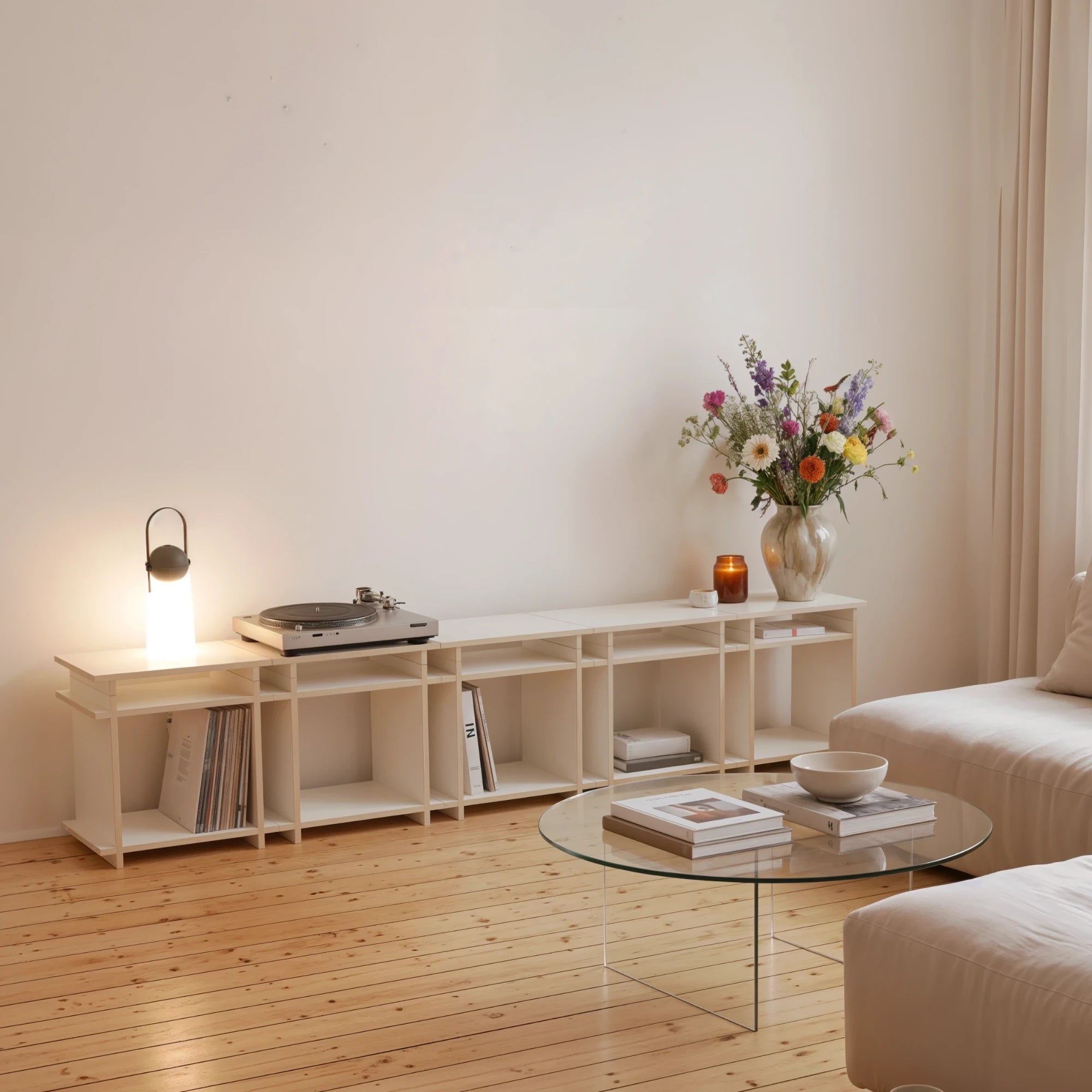 R1 Lowboard Bundle in Weiß von Kiyo mit Plattenspieler, Leuchte und Blumenstrauß im Wohnzimmer.