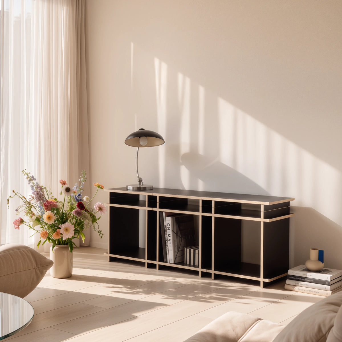 R1 TV Bundle in Schwarz von Kiyo als Sideboard im Wohnzimmer, mit Tischleuchte, Büchern und Blumenstrauß.