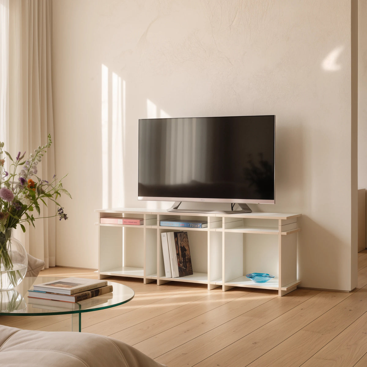 R1 TV Bundle in Weiß von Kiyo als TV-Board im Wohnzimmer, mit Fernseher, Büchern und Blumenstrauß.